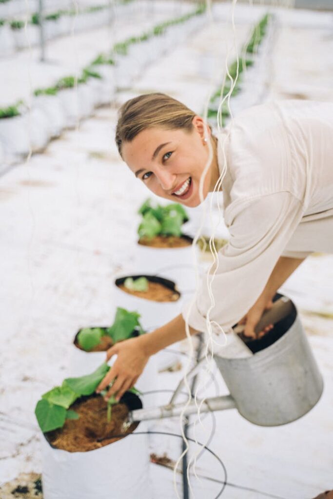 Happy woman tending plants with a watering can in a modern indoor greenhouse.
